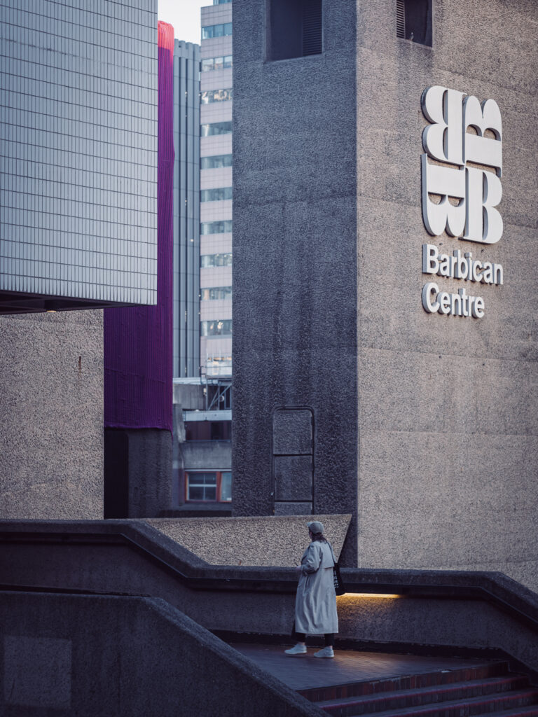 Kobieta wchodząca po schodach w barbican centre w tle brutalna architektura