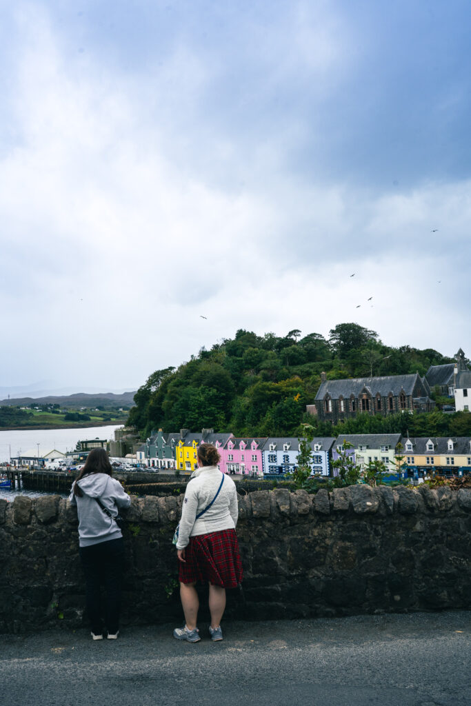 Widokówka z Portree na Isle of Skye przedstawiające kolorowe fasady budynków, port i pare podziwiającą widoki